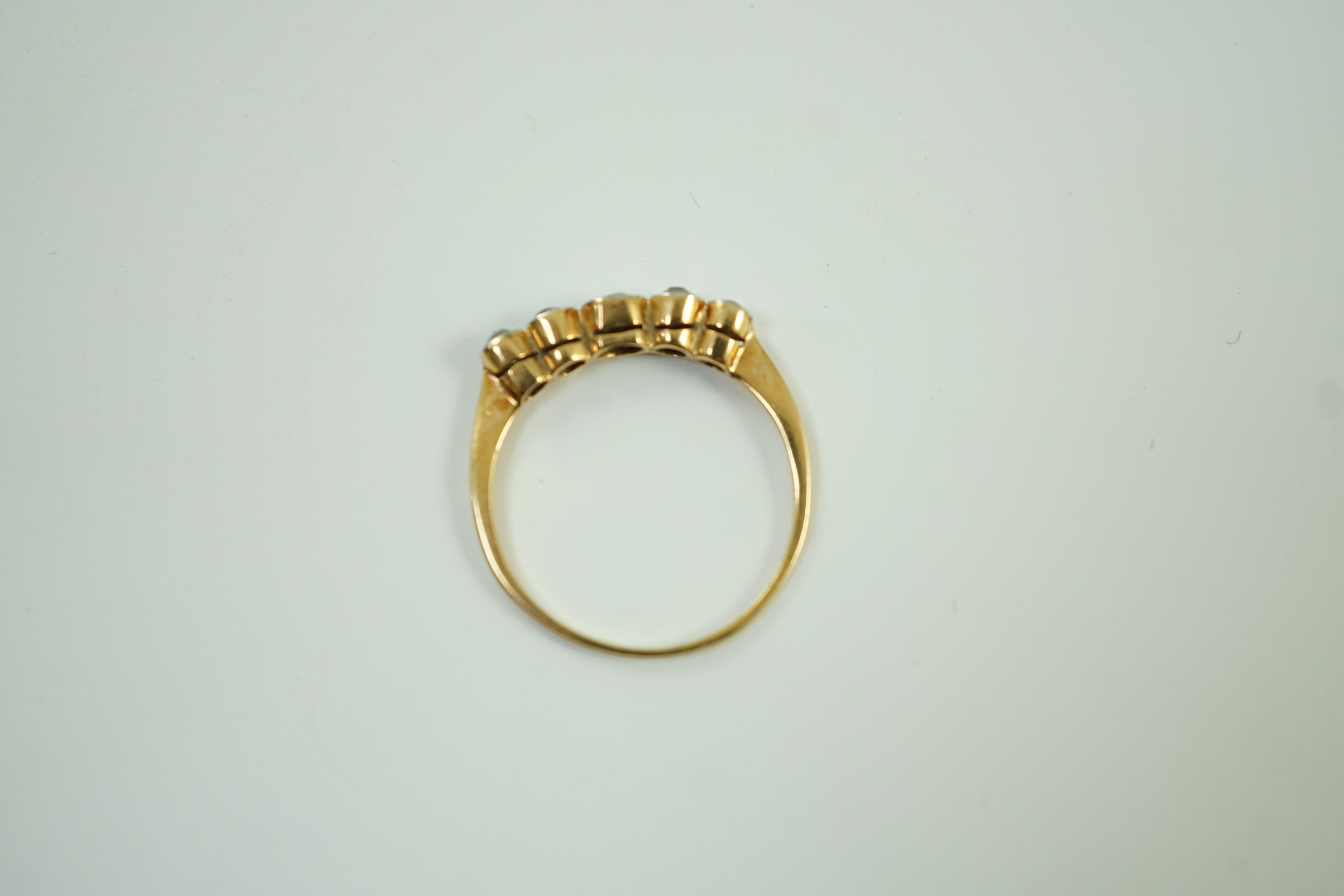 A yellow metal and graduated collet set five stone diamond half hoop ring, size V, gross weight 2.6 grams.